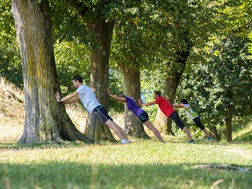 Seiser Alm Balance: active & healthy throughout spring Four people stretching against tree trunks in a park