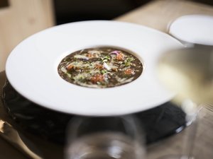 Puro gusto nel nostro ristorante a Fiè allo Sciliar Zuppa scura con erbe e pomodori in piatto bianco su base nera