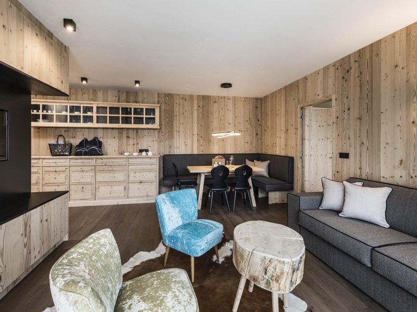 Exklusives Design: Ihre Ferienwohnung in Südtirol Gemütliches Wohnzimmer mit Holzwänden, Sofa, Stühlen und Esstisch mit Eckbank