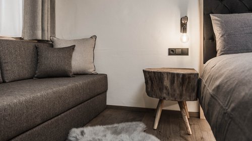 Ankommen und durchatmen: Urlaub in Völs am Schlern Gemütliche Ecke mit grauem Sofa, Holztisch und Bett im Schlafzimmer