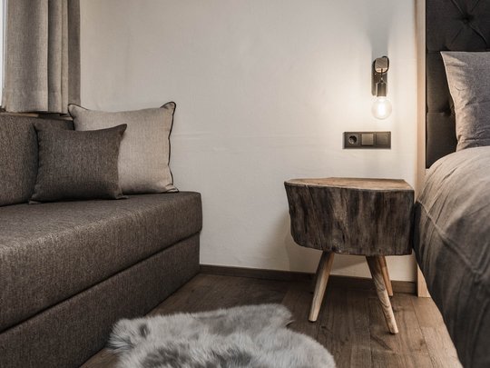 Presulis: Ihre Luxus-Ferienwohnung in Völs am Schlern Gemütliche Ecke mit grauem Sofa, Holztisch und Bett im Schlafzimmer
