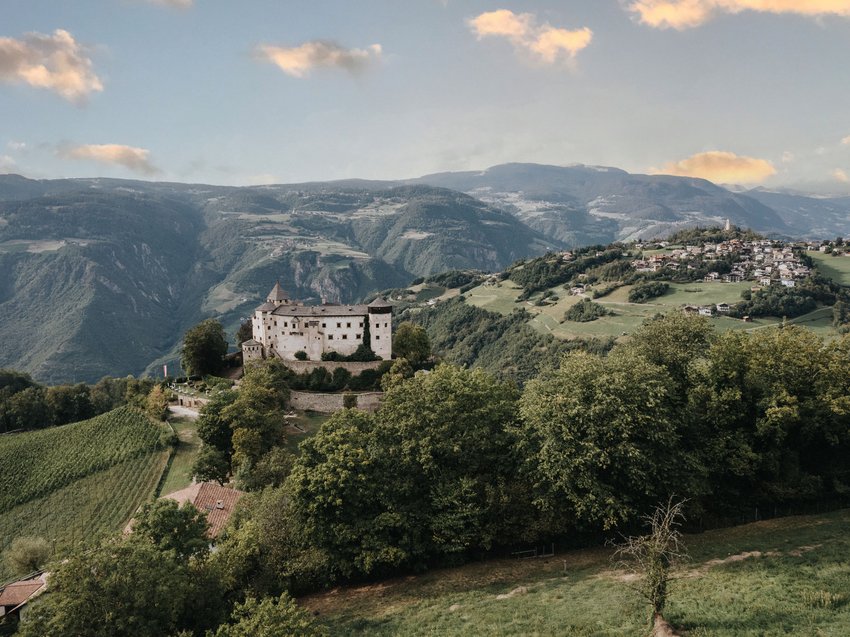 Presulis Slow hideaway: Wanderurlaub in den Dolomiten Burg auf bewaldetem Hügel mit Berglandschaft und Dorf im Hintergrund