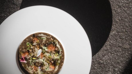 Immagini che emozionano: appartamenti Presulis a Fiè Zuppa gourmet con erbe e fiori commestibili in piatto bianco su sfondo scuro