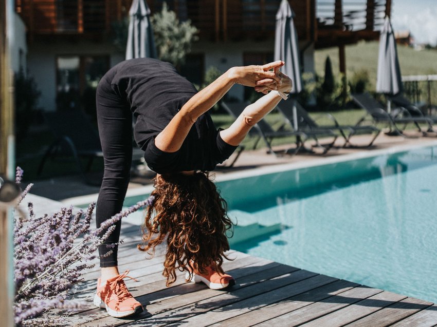 Gusto e benessere negli appartamenti con spa in montagna Donna fa stretching vicino alla piscina davanti a una casa in legno sotto il sole