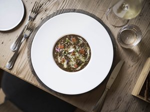 Purer Genuss in unserem Restaurant in Völs am Schlern Fein angerichteter Teller mit Pilzrisotto und Kräutern auf Holz-Tisch