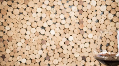 Immagini che emozionano: appartamenti Presulis a Fiè Un piatto con asparagi e un bicchiere di vino rosso davanti a una parete di tappi di sughero