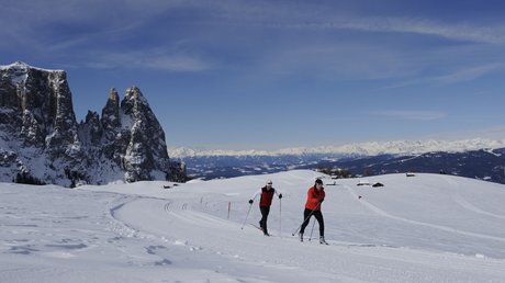Immagini che emozionano: appartamenti Presulis a Fiè Due sciatori di fondo su paesaggio nevoso montano con formazioni rocciose e cielo blu