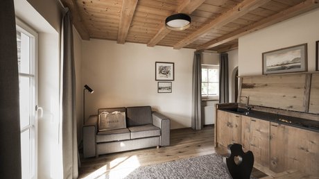 Immagini che emozionano: appartamenti Presulis a Fiè Soggiorno accogliente con divano grigio, cucina in legno e soffitto in legno