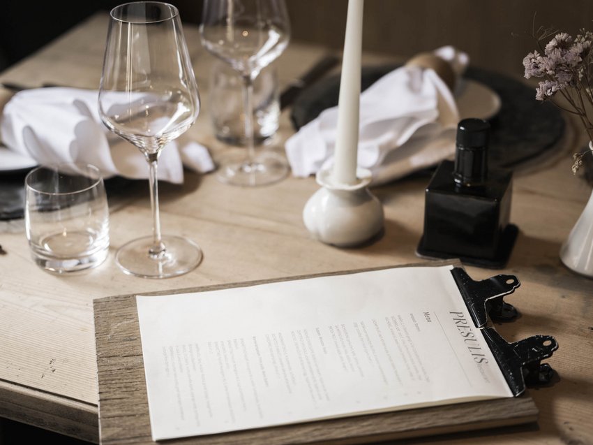 Gusto e benessere negli appartamenti con spa in montagna Tavola elegante apparecchiata con menu, candela e bicchieri