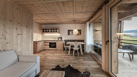 Immagini che emozionano: appartamenti Presulis a Fiè Soggiorno con soffitto in legno, angolo cottura, tavolo da pranzo e porta scorrevole in vetro verso il balcone