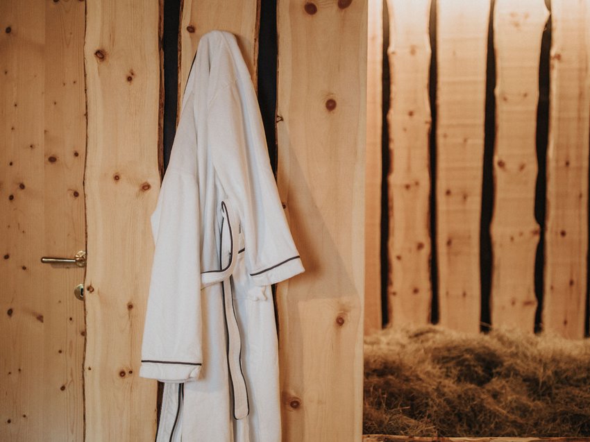 Presulis: Ihre Luxus-Ferienwohnung in Völs am Schlern Weißer Bademantel hängt an Holzwand neben Holzbett mit Heu