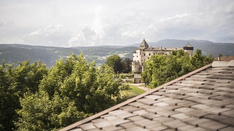 Bilder, die begeistern: Presulis Hideaway Apartments & Restaurant in Völs Historisches Schloss hinter grünen Bäumen und einer Dachterrasse mit Bergen im Hintergrund