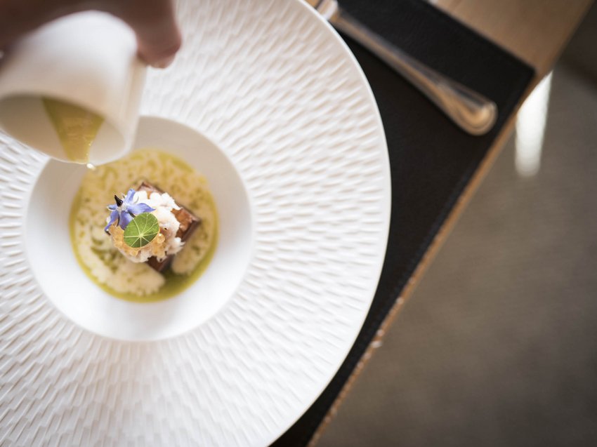 The Presulis: discover and experience South Tyrol Hand pouring sauce over a gourmet dish garnished with edible flowers