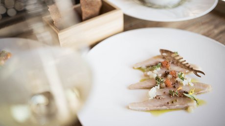 Immagini che emozionano: appartamenti Presulis a Fiè Antipasto di pesce finemente impiattato con erbe e fiori commestibili su piatto bianco