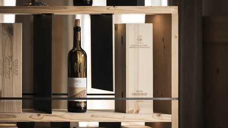 Immagini che emozionano: appartamenti Presulis a Fiè Bottiglia di vino e scatole di legno su scaffale in ambiente con luce calda