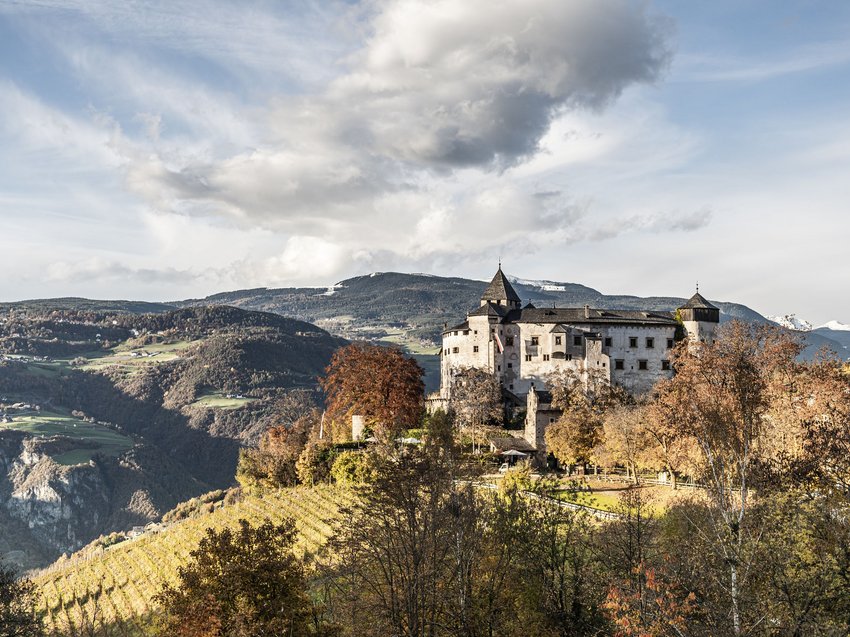 Albergatori per passione, una lunga tradizione d’ospitalità Castello su una collina autunnale con paesaggio montano e cielo nuvoloso