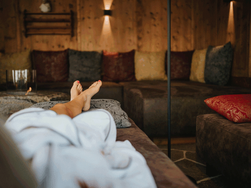 Ankommen und durchatmen: Urlaub in Völs am Schlern Person entspannt sich in Bademantel auf Sofa in gemütlichem Raum