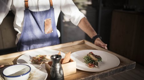 Immagini che emozionano: appartamenti Presulis a Fiè Cameriere porta un vassoio con cibo raffinato, fette di pane e contenitore nero