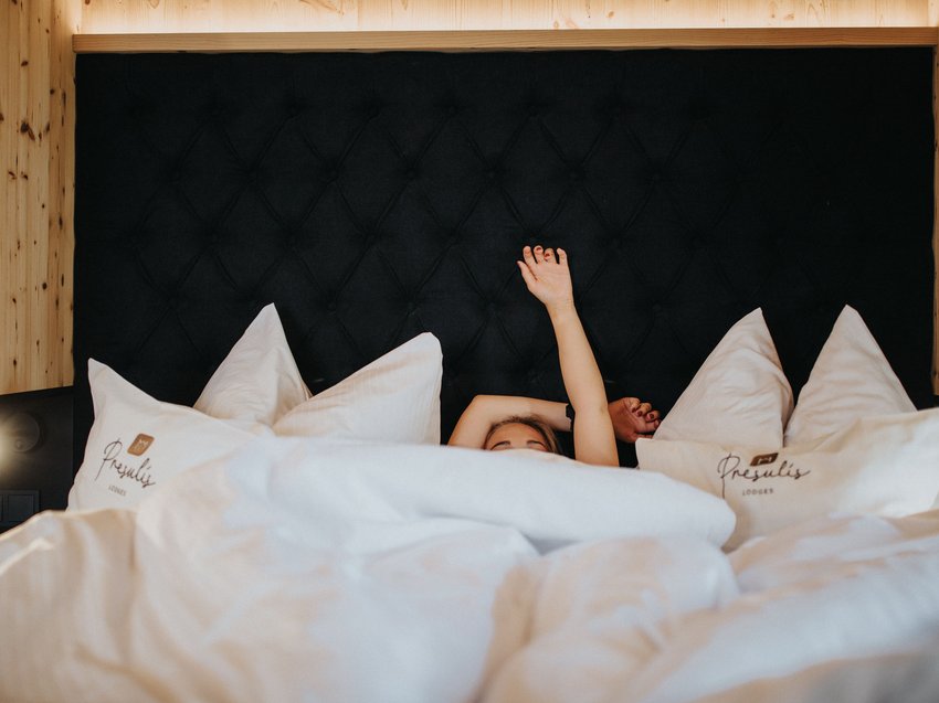 Exklusives Design: Ihre Ferienwohnung in Südtirol Person liegt im Bett mit weißen Kissen und hebt einen Arm nach oben