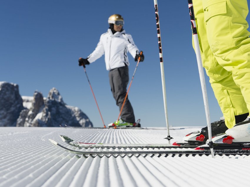 A winter holiday on the Alpe di Suisi/Seiser Alm Skiers on freshly groomed slope with mountain backdrop under clear sky