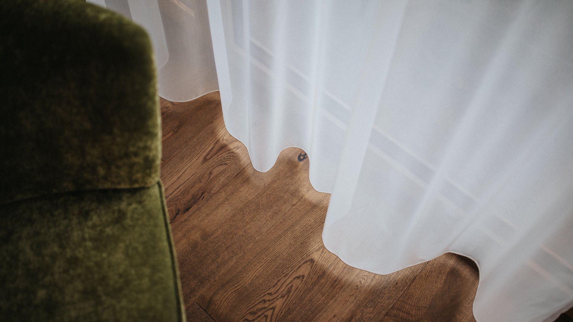 White curtain over wooden floor next to green furniture piece