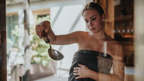 Immagini che emozionano: appartamenti Presulis a Fiè Donna in sauna versa acqua sulle pietre calde