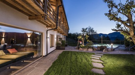 Immagini che emozionano: appartamenti Presulis a Fiè Giardino moderno con piscina, sentiero di pietra e casa illuminata al crepuscolo