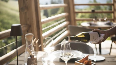 Immagini che emozionano: appartamenti Presulis a Fiè Vino versato su un tavolo di legno apparecchiato con cibo su una terrazza aperta