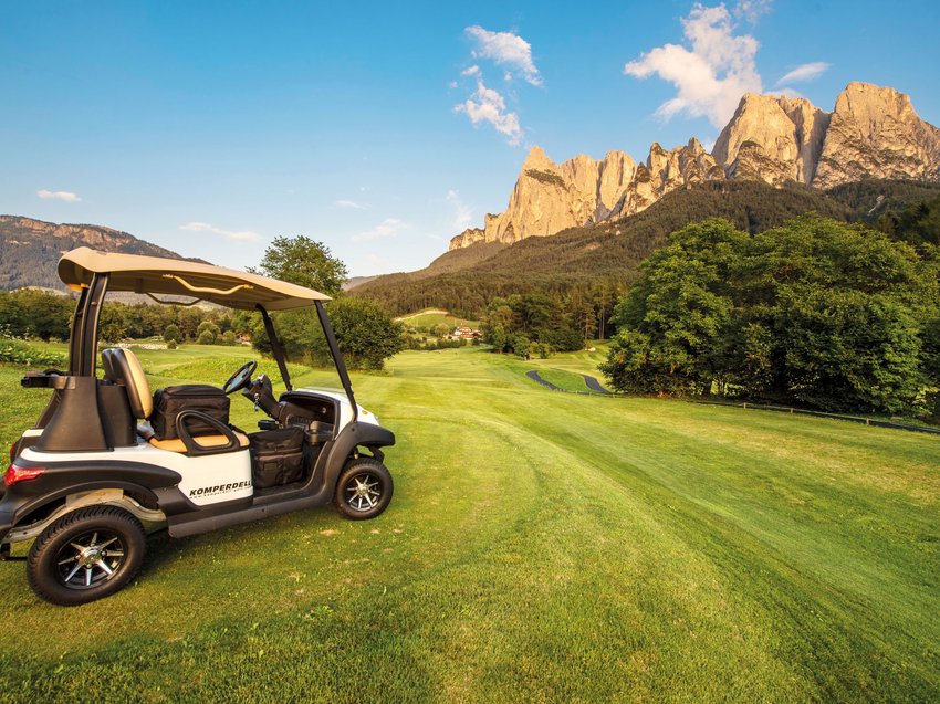 Presulis luxury apartments: your golf holiday in South Tyrol Golf cart on green golf course with mountain view at sunset