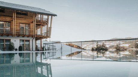 Immagini che emozionano: appartamenti Presulis a Fiè Casa in legno accanto a piscina calma con vista sulle montagne e cielo limpido