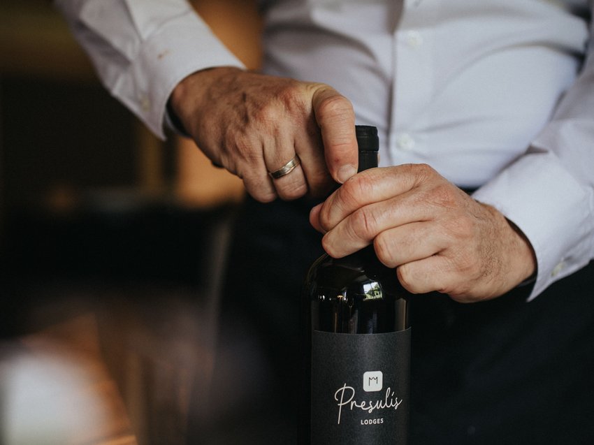 Presulis: degustazioni di vini in Alto Adige Persona che apre una bottiglia di vino con etichetta nera su tavolo apparecchiato