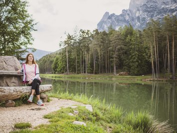 Seiser Alm Balance: active & healthy throughout spring Woman sitting on a wooden bench by a lake with forest and mountains in background