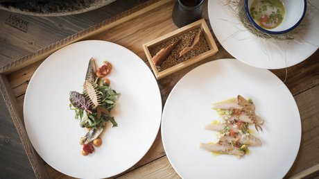 Immagini che emozionano: appartamenti Presulis a Fiè Due piatti di pesce artisticamente impiattati su un vassoio di legno