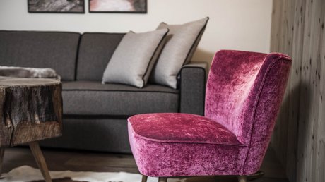 Immagini che emozionano: appartamenti Presulis a Fiè Sedia in velluto rosa davanti a divano grigio con cuscini e tavolo rustico