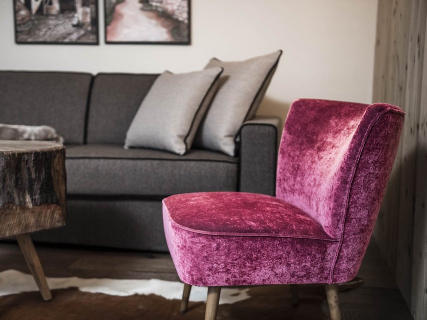 Presulis: Ihre Luxus-Ferienwohnung in Völs am Schlern Rosa Samtstuhl vor grauem Sofa mit Kissen und rustikalem Holztisch