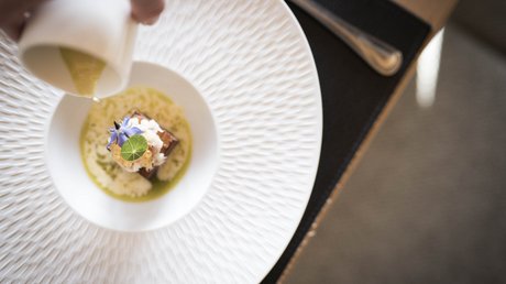 Immagini che emozionano: appartamenti Presulis a Fiè Mano versa salsa su piatto finemente impiattato in piatto bianco